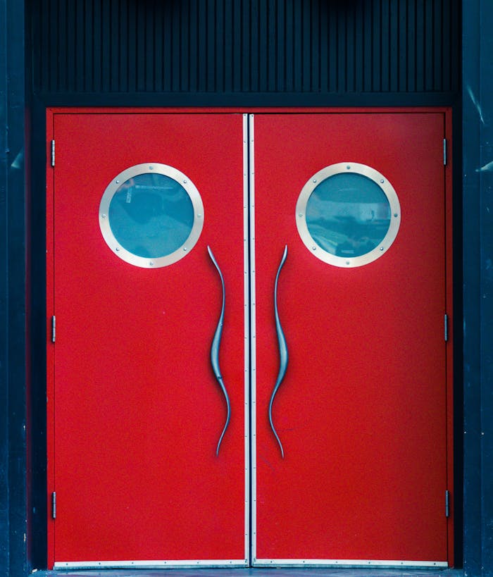gallery-5 Close-up of a red double door featuring round windows and sleek handles.