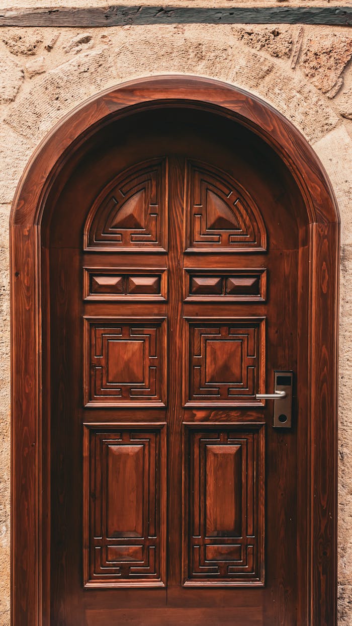 gallery-3 A beautifully crafted wooden door with intricate patterns set in an arched stone frame.