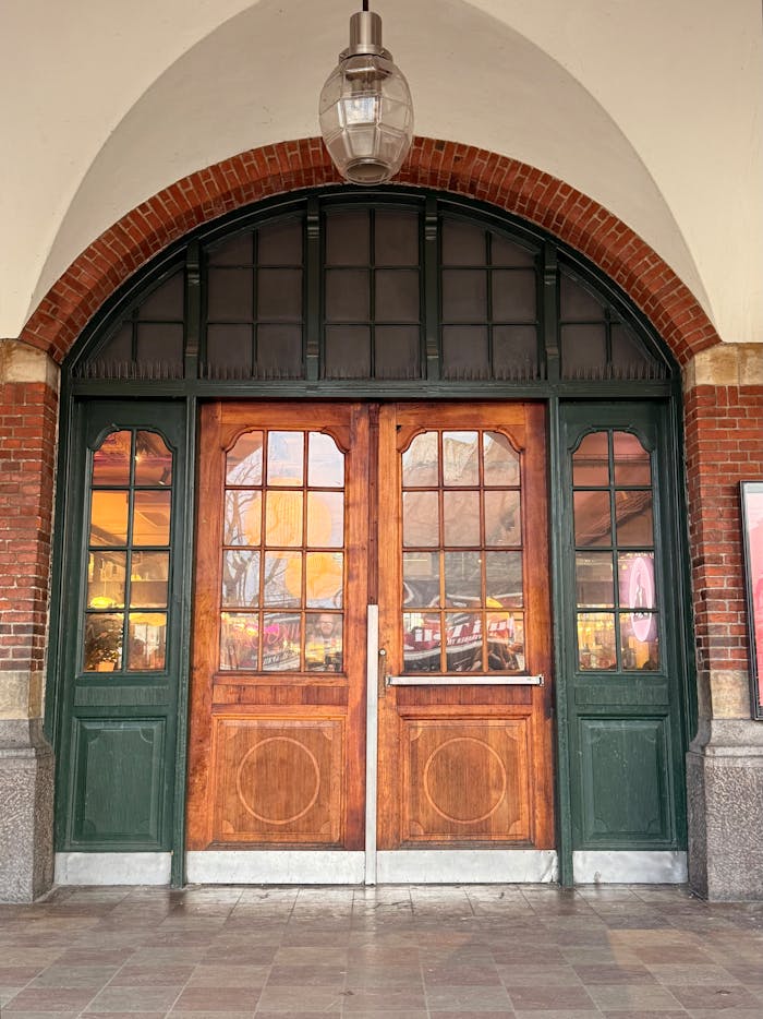 A pair of rustic wooden double doors set in a vintage brick archway.