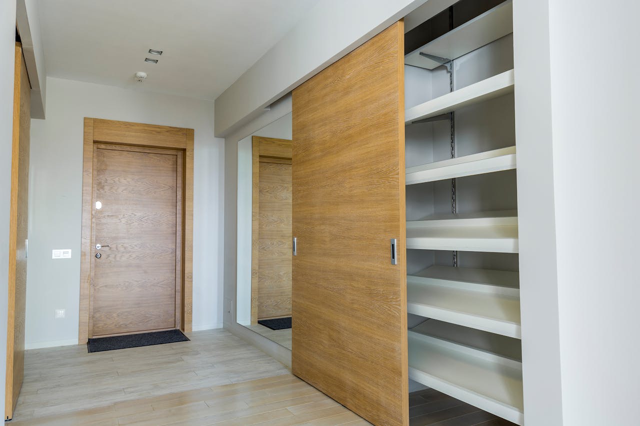 hero-img-01 Elegant modern walk-in closet with wooden sliding door and empty shelves in a sleek minimalist style.